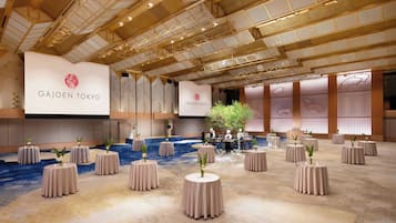 A spacious banquet hall with round tables, a stage, and a ceiling with a geometric design.