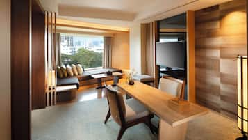 A modern hotel room with a sofa set, a dining table, a TV, and a view of the cityscape.