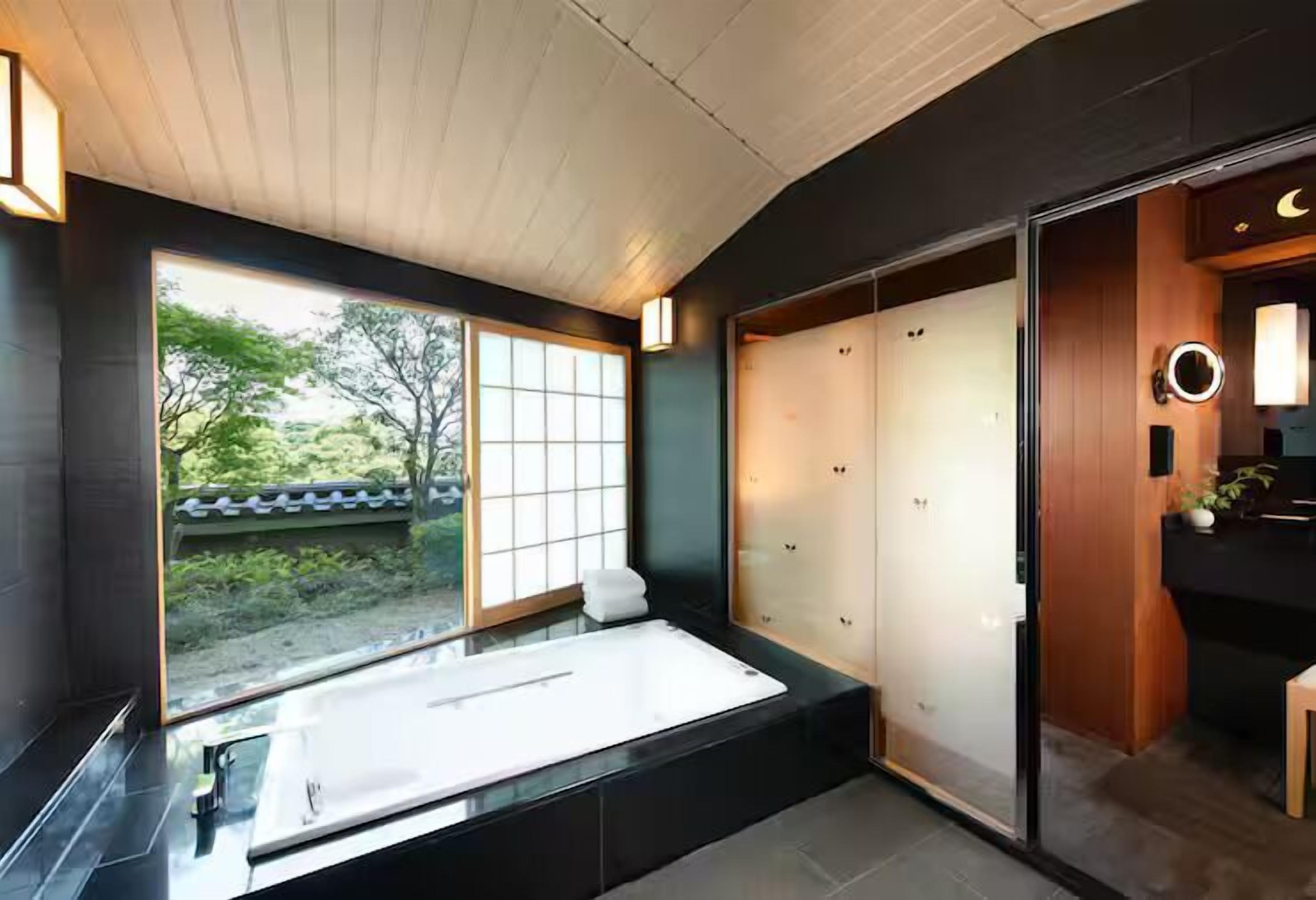 A modern bathroom with a large bathtub, sliding doors, and a view of a garden.