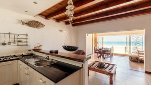 A kitchen with a large island, wooden ceiling beams, and a view of the beach through open doors. - Clef des Iles (Mahé Island)