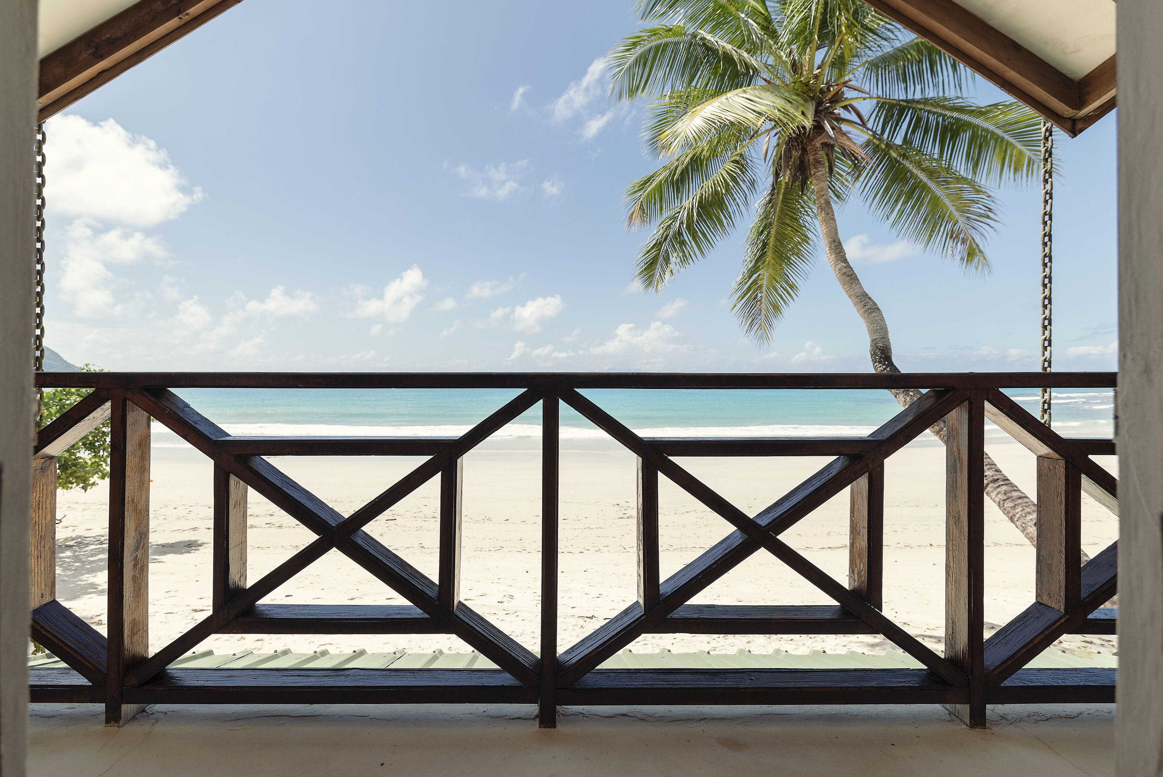 Un balcón de madera con vista a una playa y una palmera.
