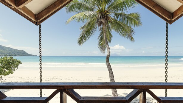 A wooden deck with a view of a beach and a palm tree. - Clef des Iles (Mahé Island)