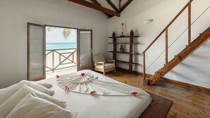 A bedroom with a bed, a chair, a wooden staircase, and a view of the beach. - Clef des Iles (Mahé Island)
