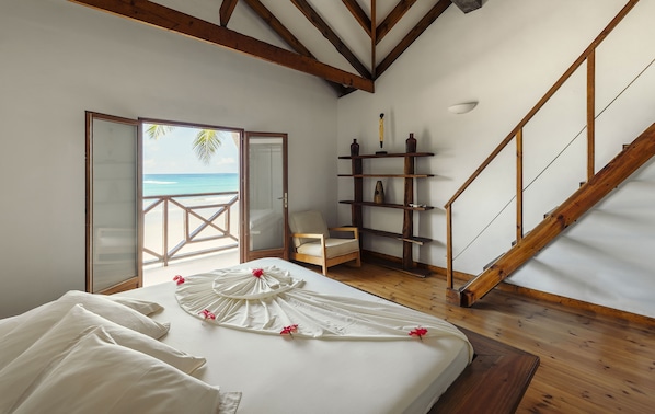 A bedroom with a bed, a chair, a wooden staircase, and a view of the beach. - Clef des Iles (Mahé Island)