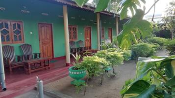 A green building with wooden doors and windows, a covered porch with chairs, and potted plants.