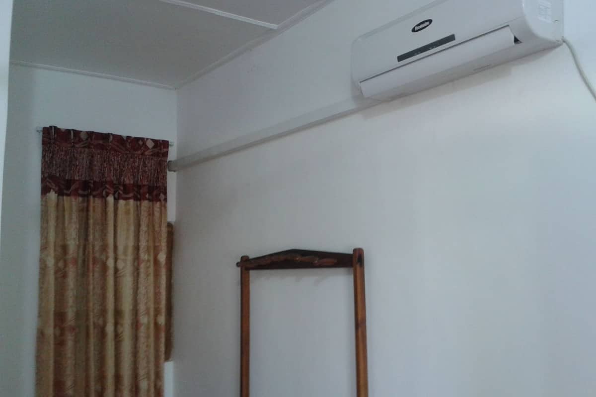 Una habitación con techo blanco, pared blanca, una ventana con cortina estampada y una silla de madera.