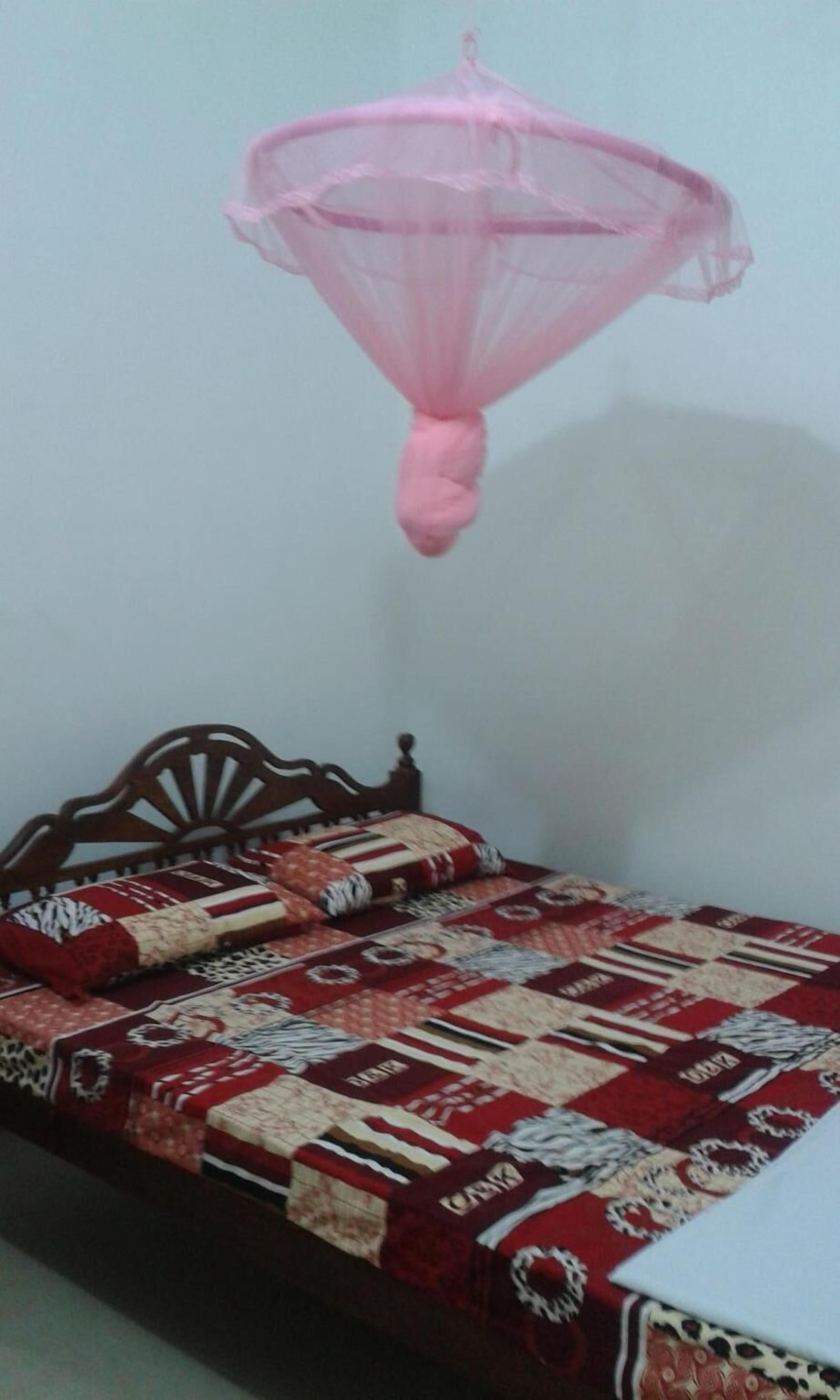 A bed with a patterned bedspread and a pink mosquito net hanging above it.