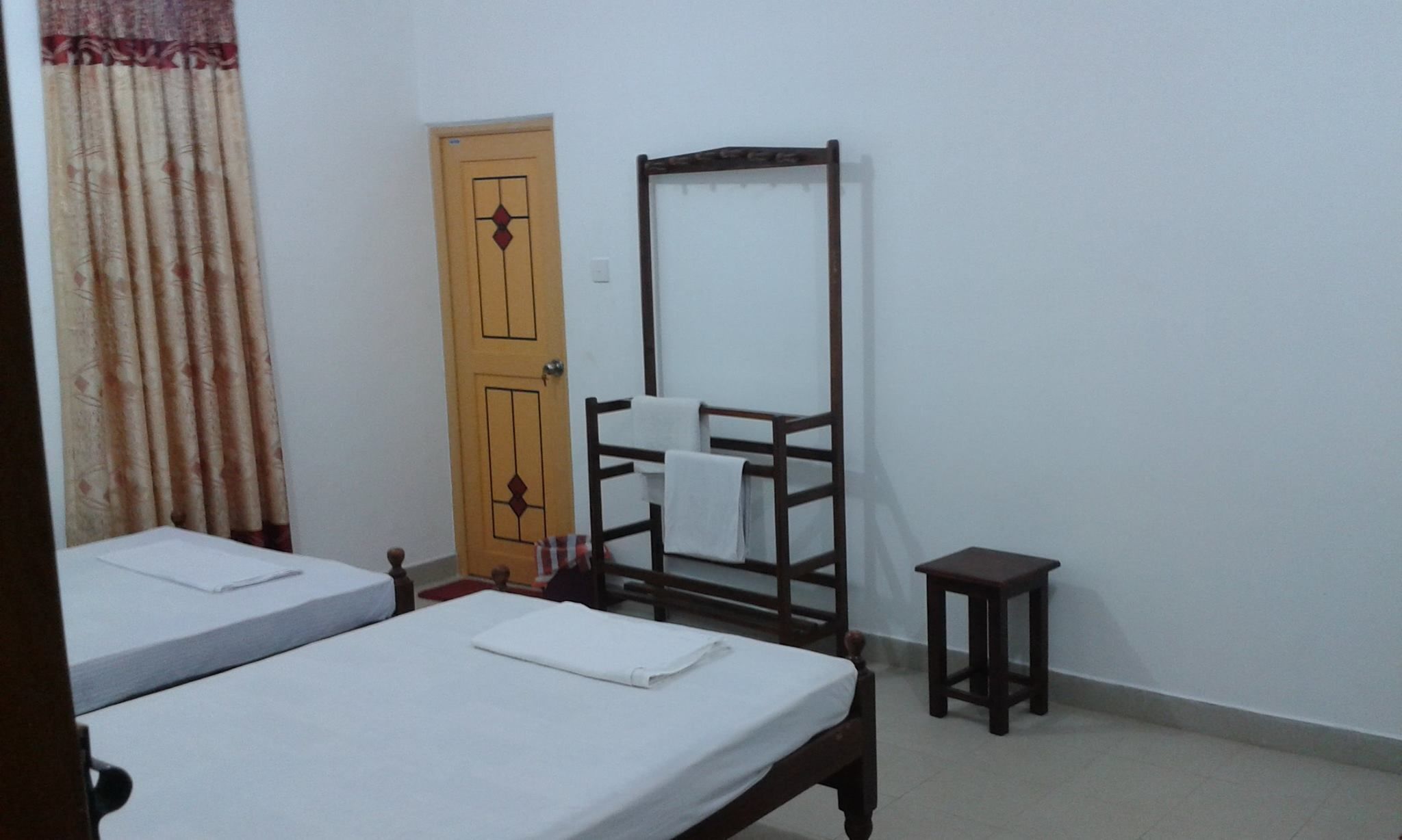 Une chambre avec deux lits, une armoire en bois, une petite table et une porte ornée d’un panneau décoratif.
