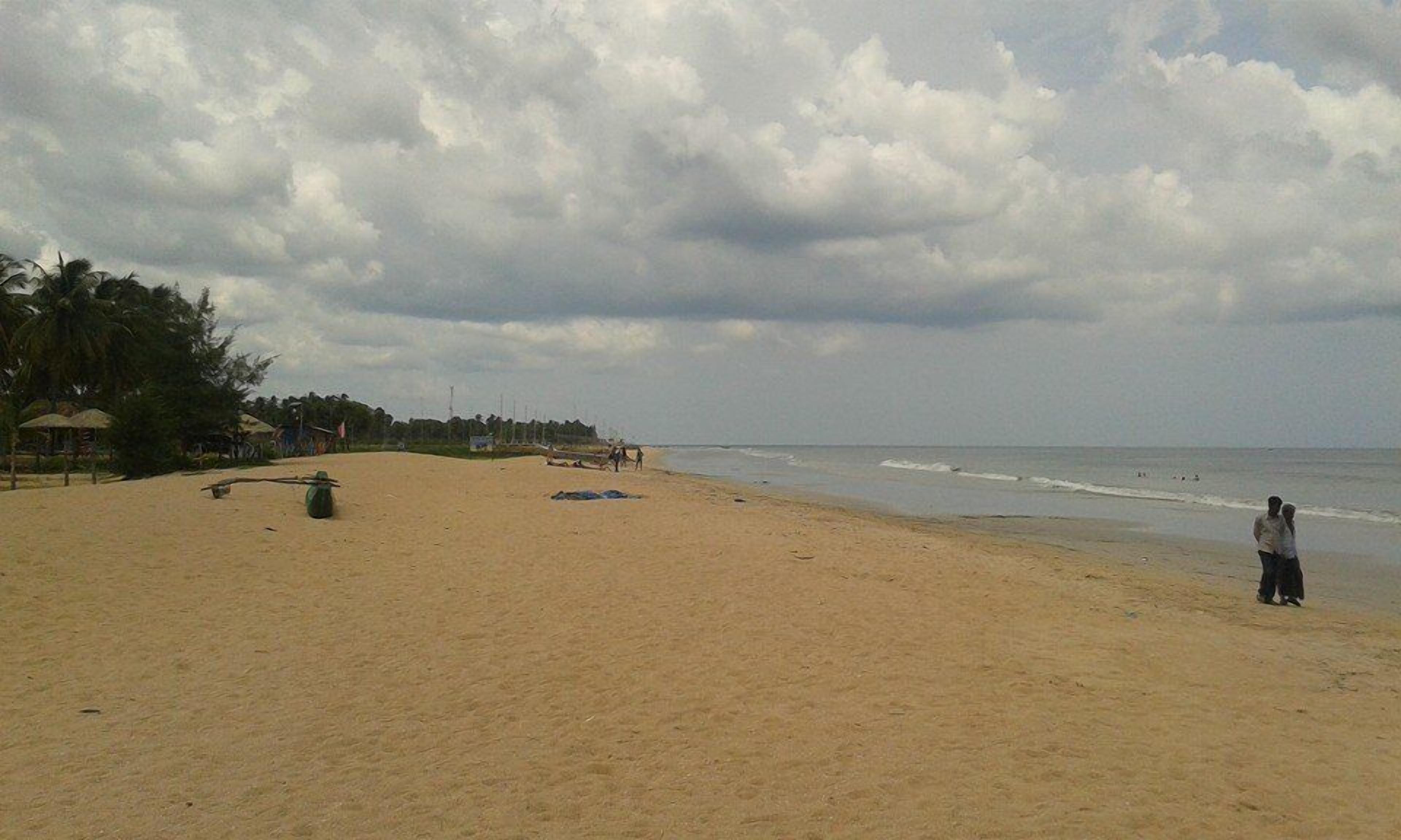 Una playa con arena, algunas personas y construcciones al fondo.