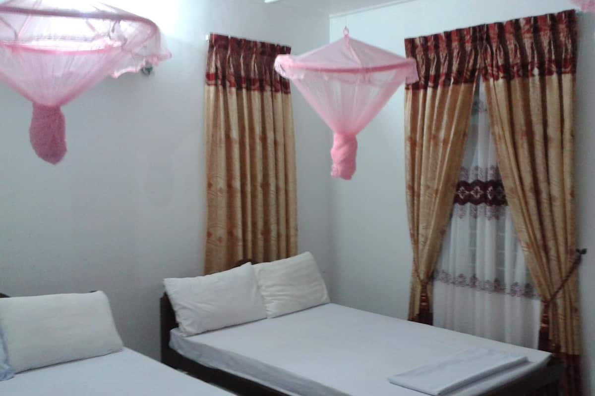 Un dormitorio con dos camas individuales, una ventana con cortinas estampadas y una mosquitera sobre una de las camas.
