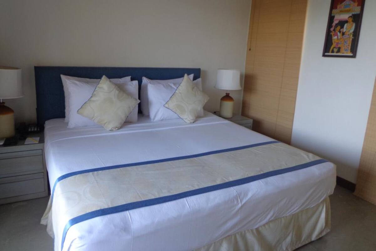 A neatly made bed with a blue stripe, two bedside lamps, and a wall with a framed picture.