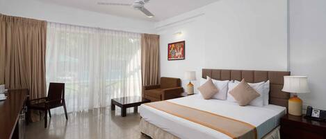 A hotel room with a large bed, a desk, a chair, a sofa, a ceiling fan, and a window with curtains.