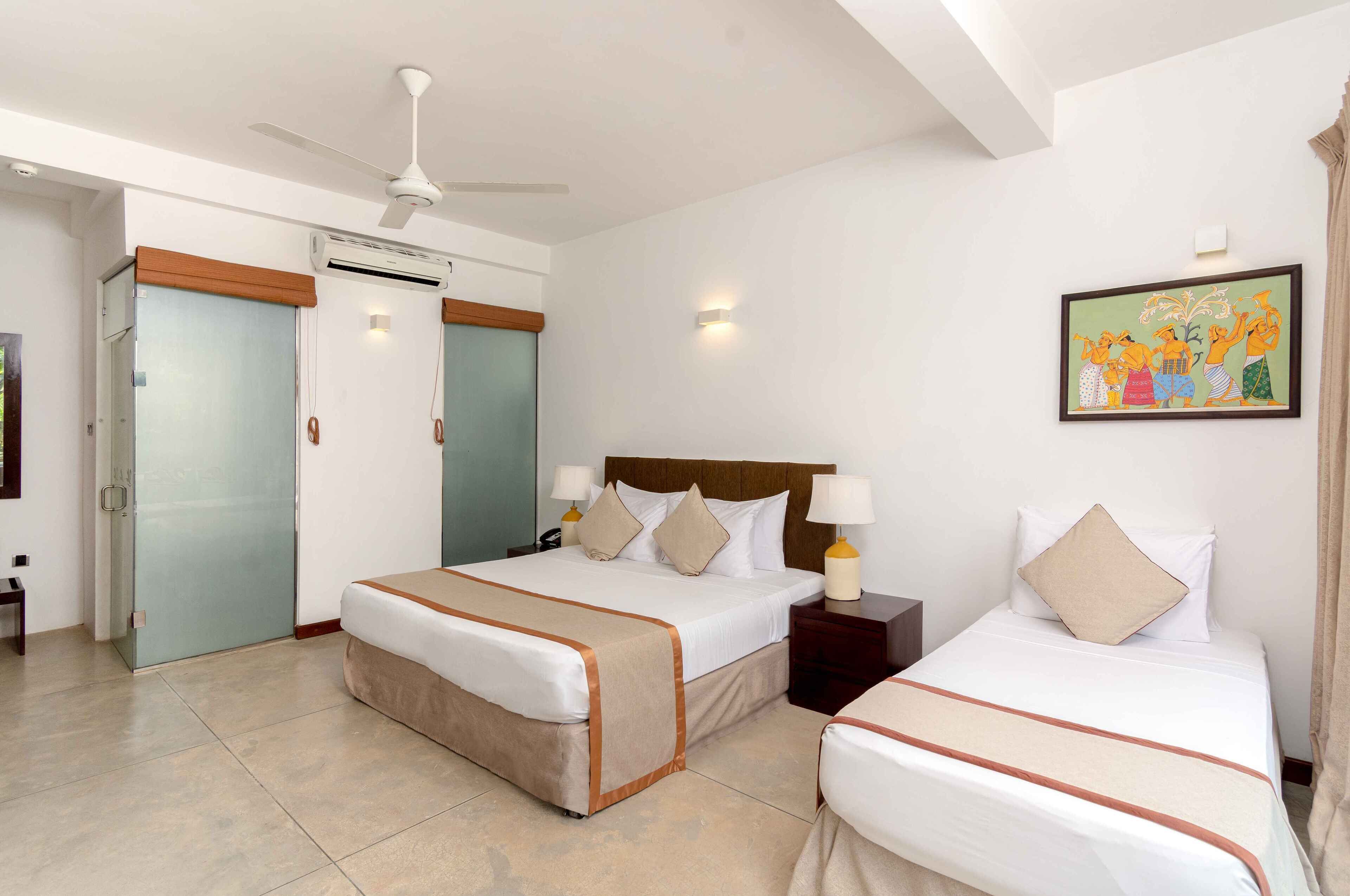 A hotel room with a bed, bedside tables, a ceiling fan, an air conditioning unit, a door, and a wall-mounted artwork.