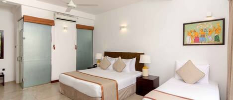 A hotel room with a bed, bedside tables, a ceiling fan, an air conditioning unit, a door, and a wall-mounted artwork.