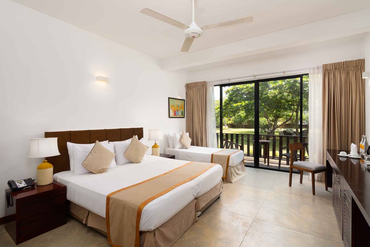 A hotel room with two beds, a desk, a chair, a balcony, and a ceiling fan.