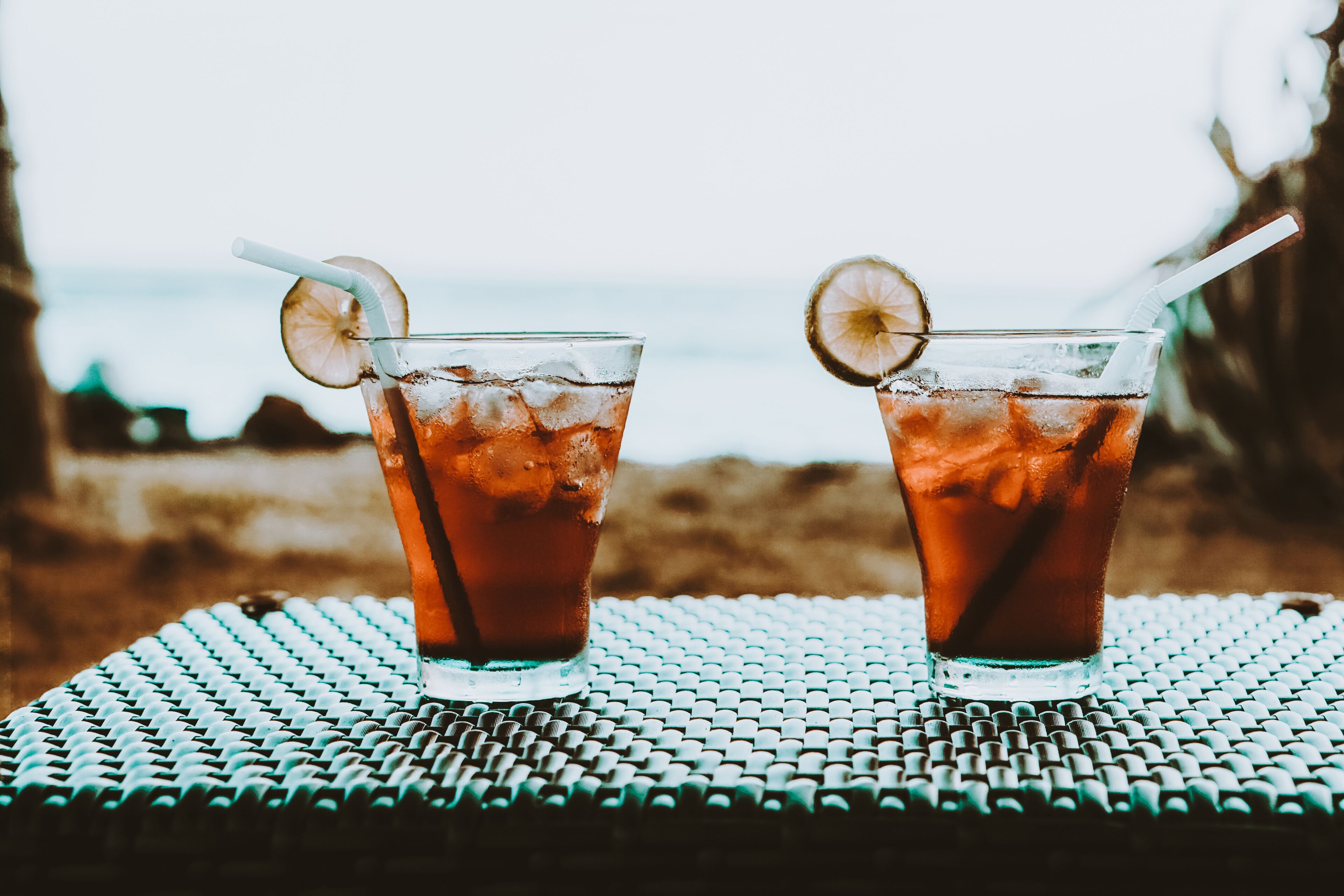 Two glasses of iced tea on a textured table with a blurred beach and ocean in the background.