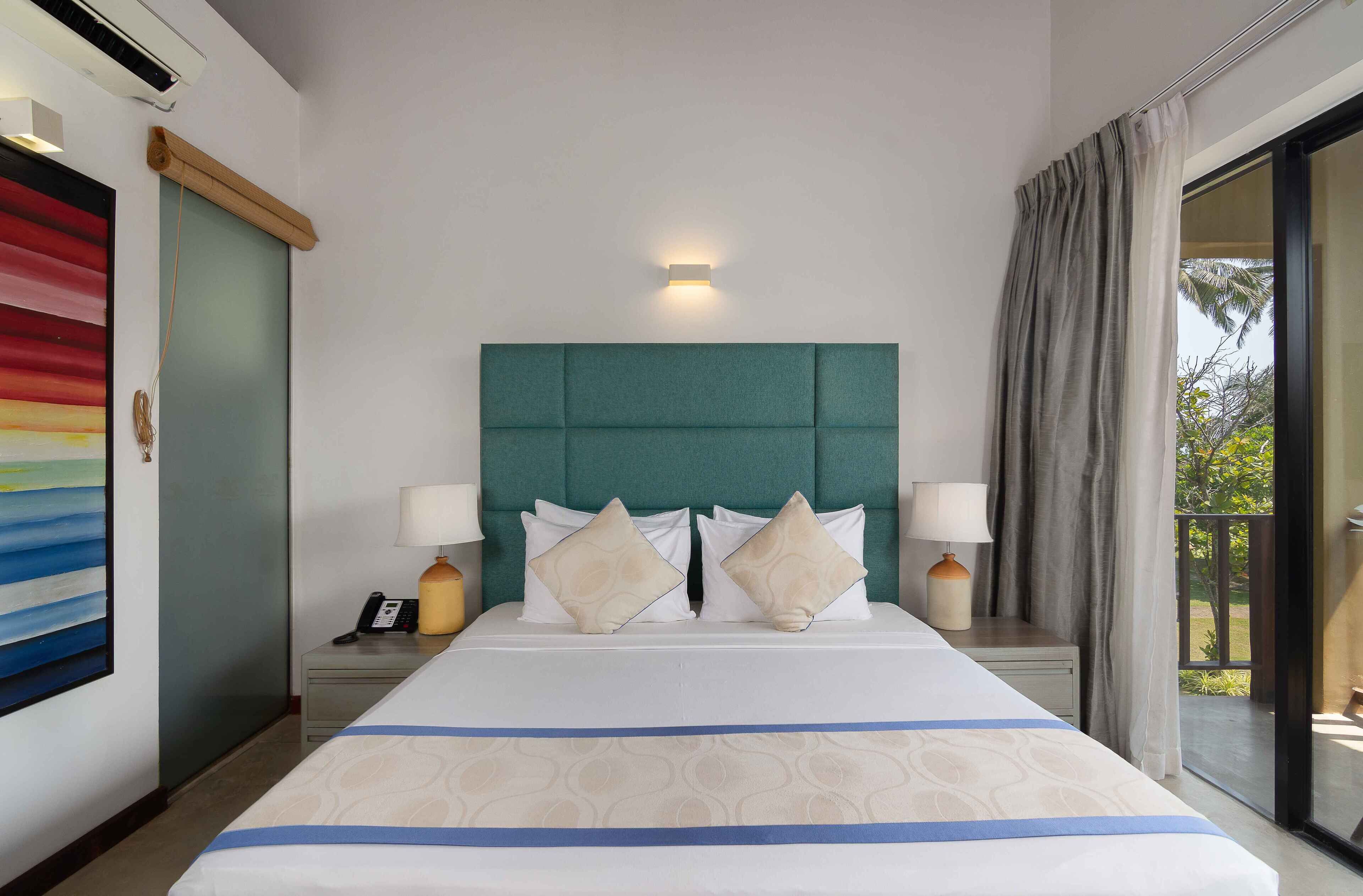 Una habitación de hotel con una cama grande, un cabecero, dos mesitas de noche con lámparas, un teléfono y vistas al exterior.