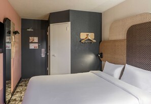 Hotellihuone, jossa on sänky, vaatekaappi, peili ja seinälle kiinnitetty henkariteline.