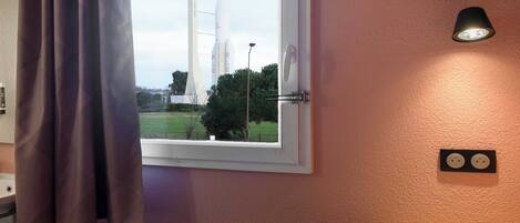 A room with a window, a wall-mounted light fixture, and a wall socket.