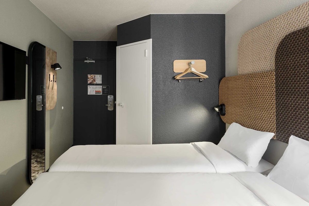 A hotel room with a bed, a wardrobe, a mirror, a wall-mounted light, and a hanging coat rack.