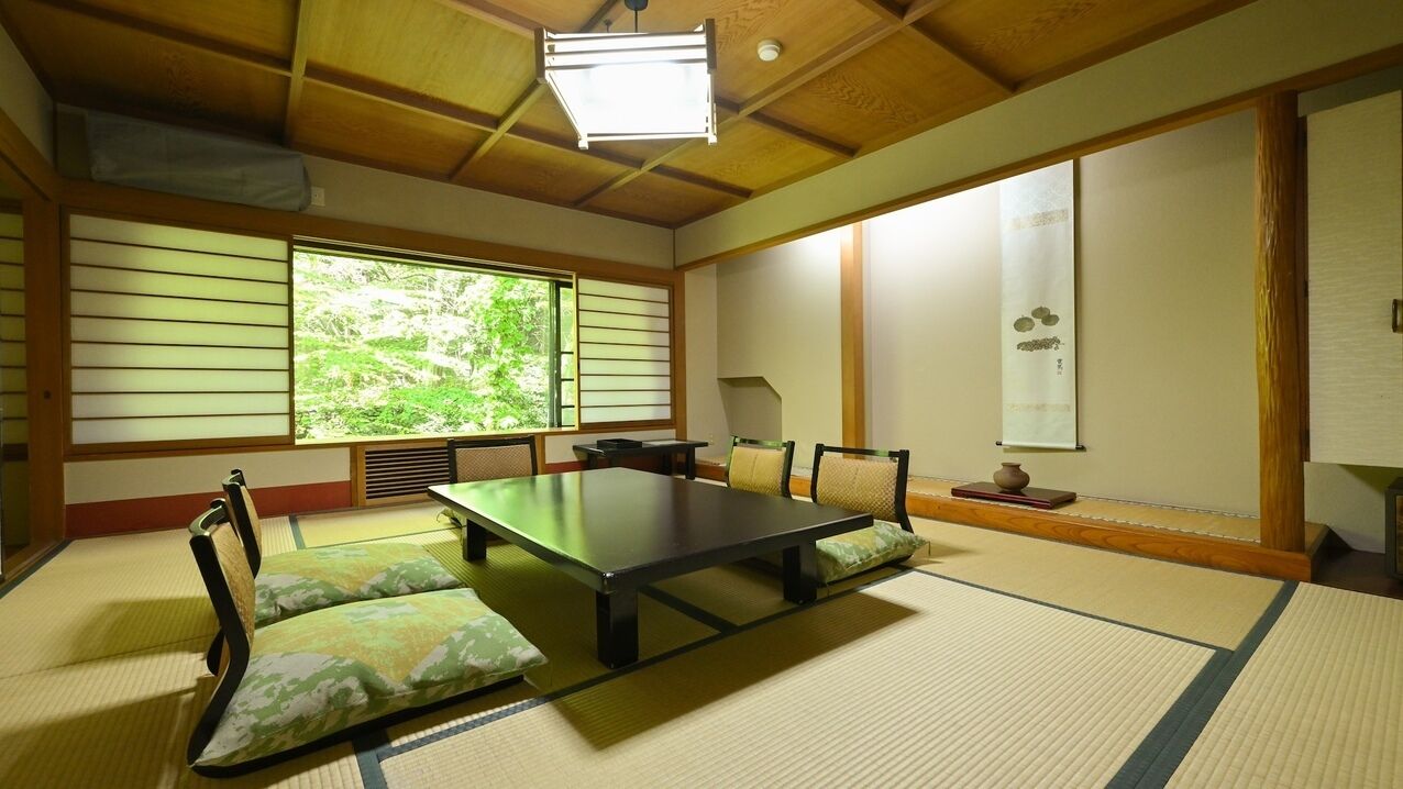 Een traditionele Japanse kamer met tatami vloerbedekking, een lage tafel, kussens, schuifdeuren en uitzicht op groen.