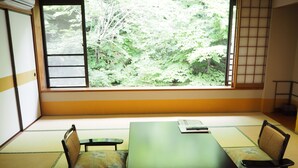Una habitación con tatamis, una mesa baja, dos sillas y vistas a un bosque a través de un ventanal grande.