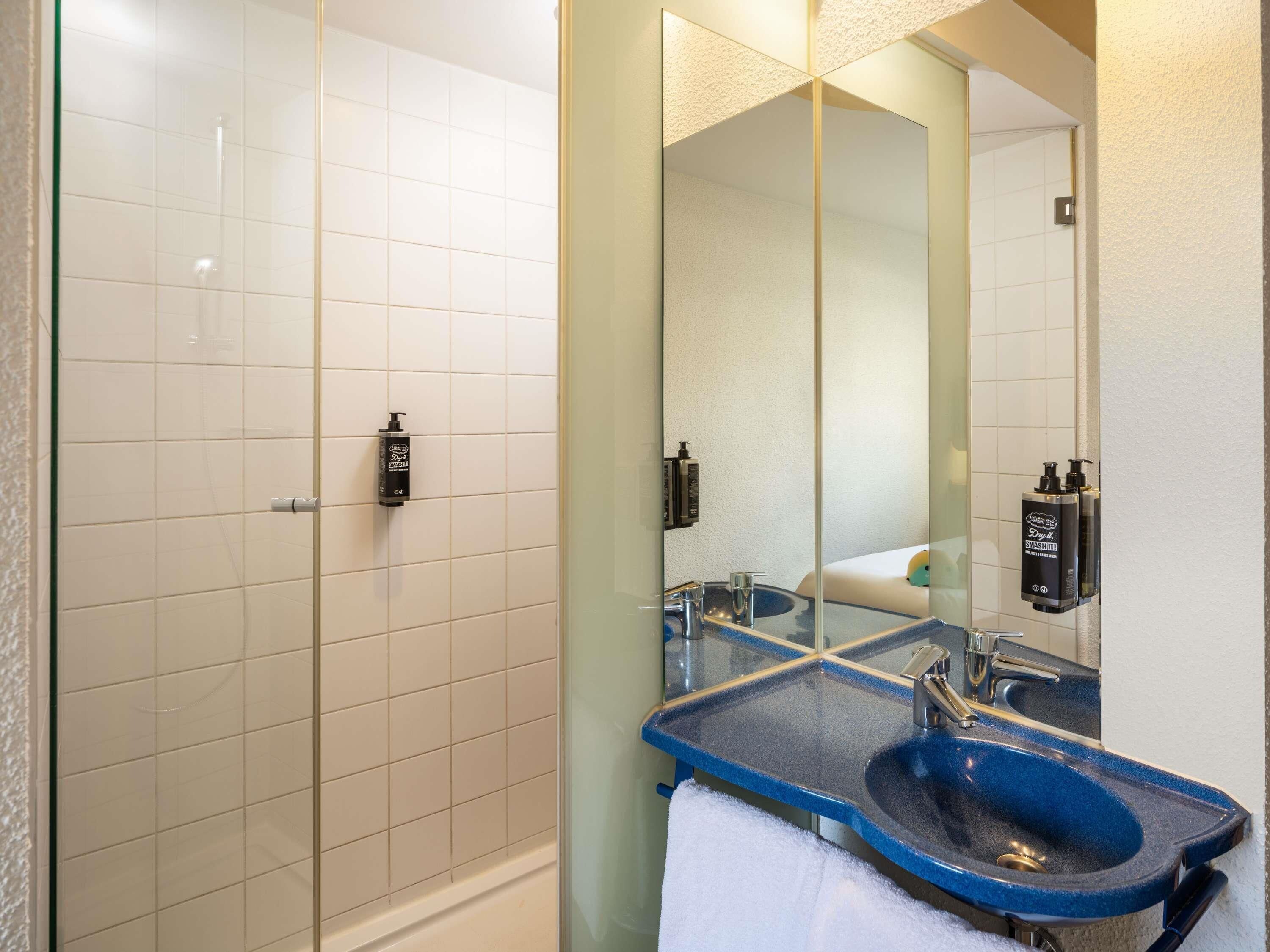 A bathroom with a glass shower enclosure, a blue sink, and a large mirror.