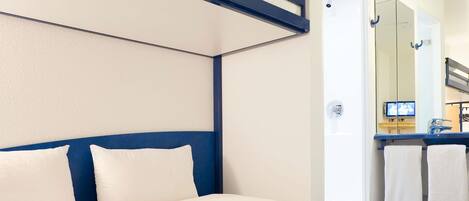 A hotel room with a bed, a mirror, a TV, and a bathroom visible through the door.
