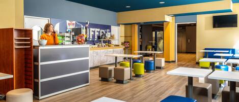 A modern cafe with a counter, seating area, and a staircase leading to another level.