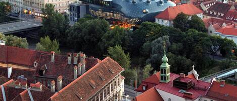 A cityscape with historic buildings, a prominent modern structure with a unique roof, and a green-roofed church.
