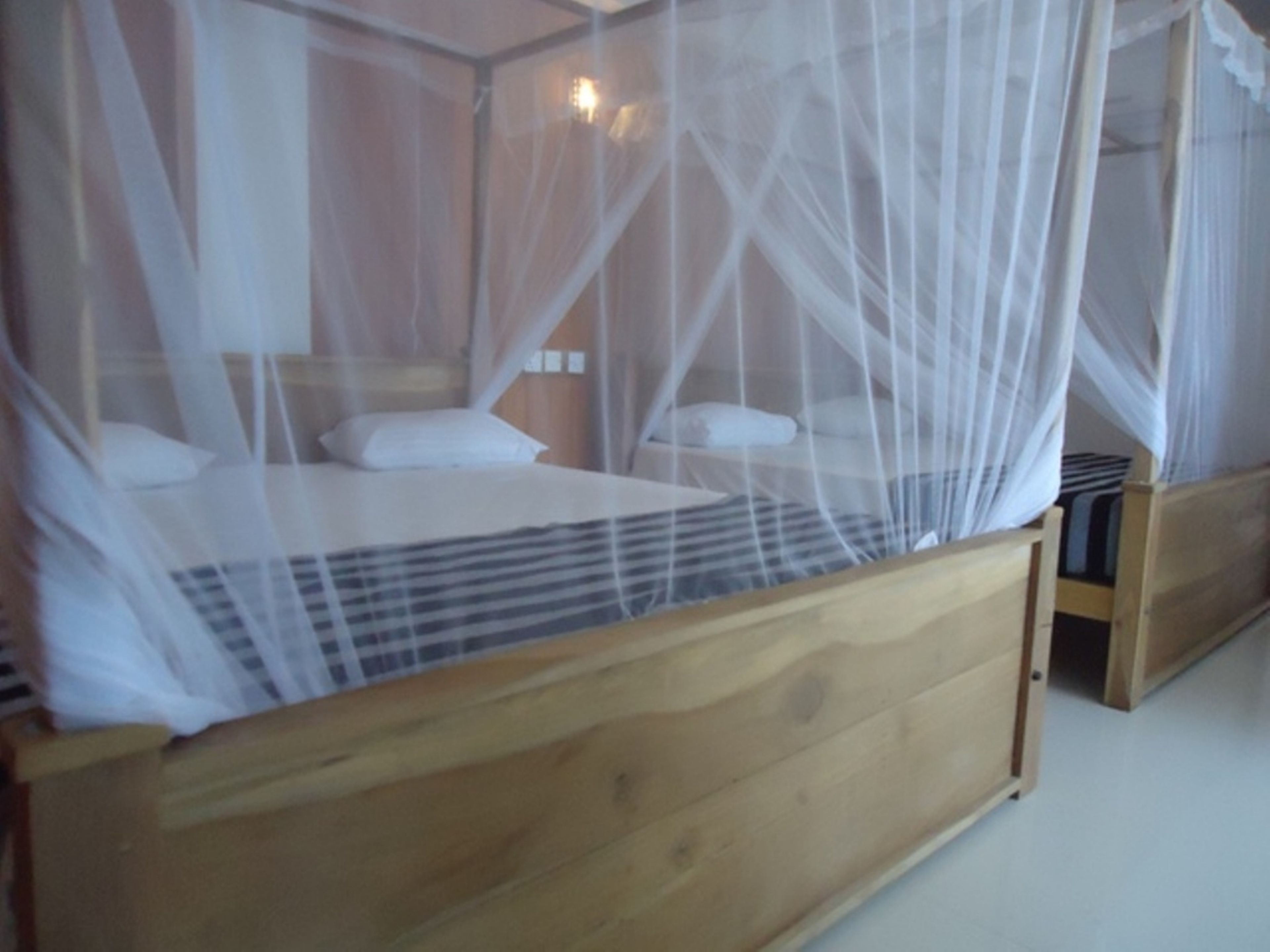 Una cama de madera con dosel, almohadas blancas y colcha a rayas.