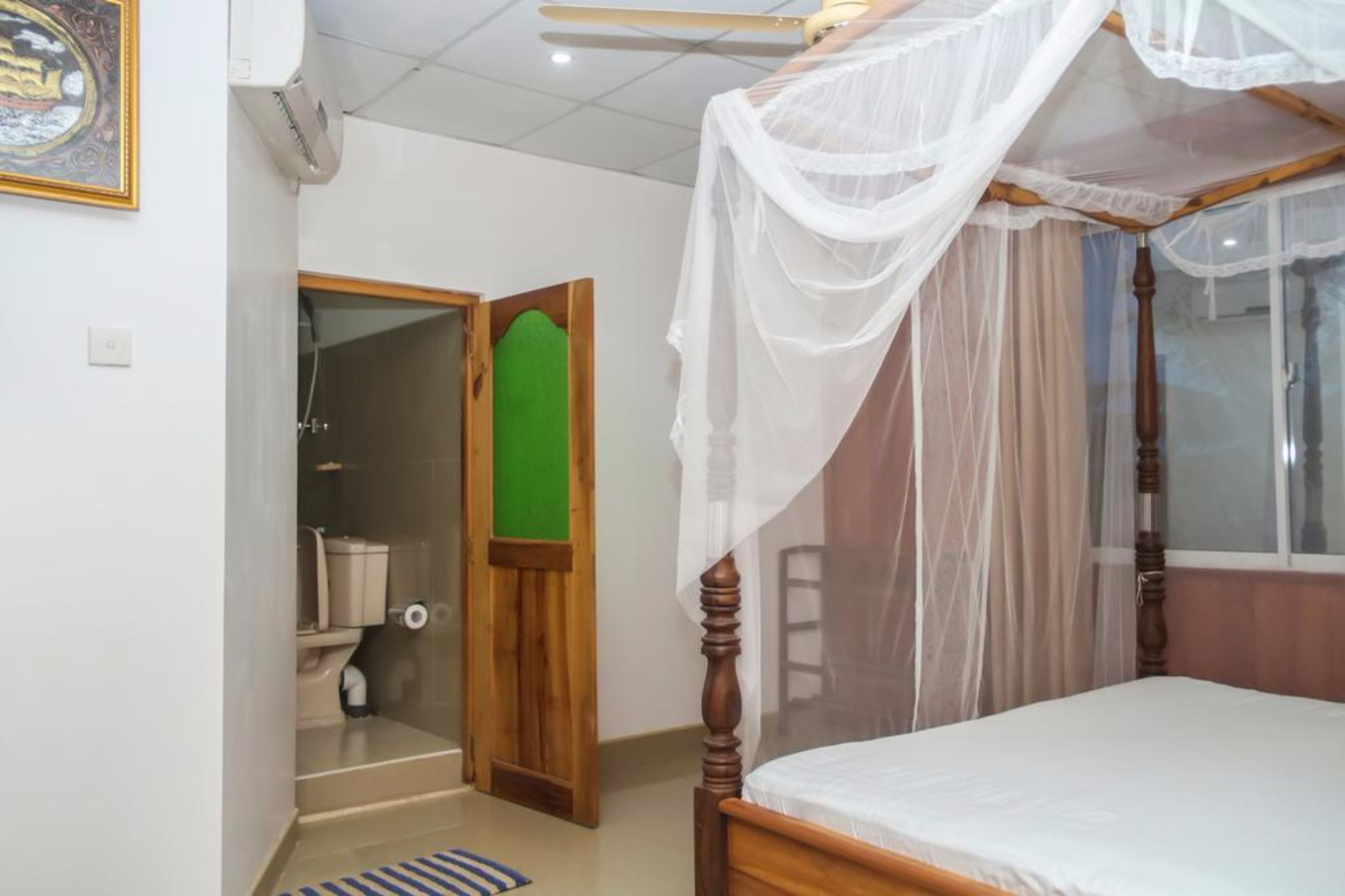 A bedroom with a wooden bed, a canopy, a green door, and a white toilet visible through an open door.