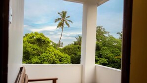 A balcony with a wooden bench and a small table, overlooking a lush green landscape with trees and a palm tree.