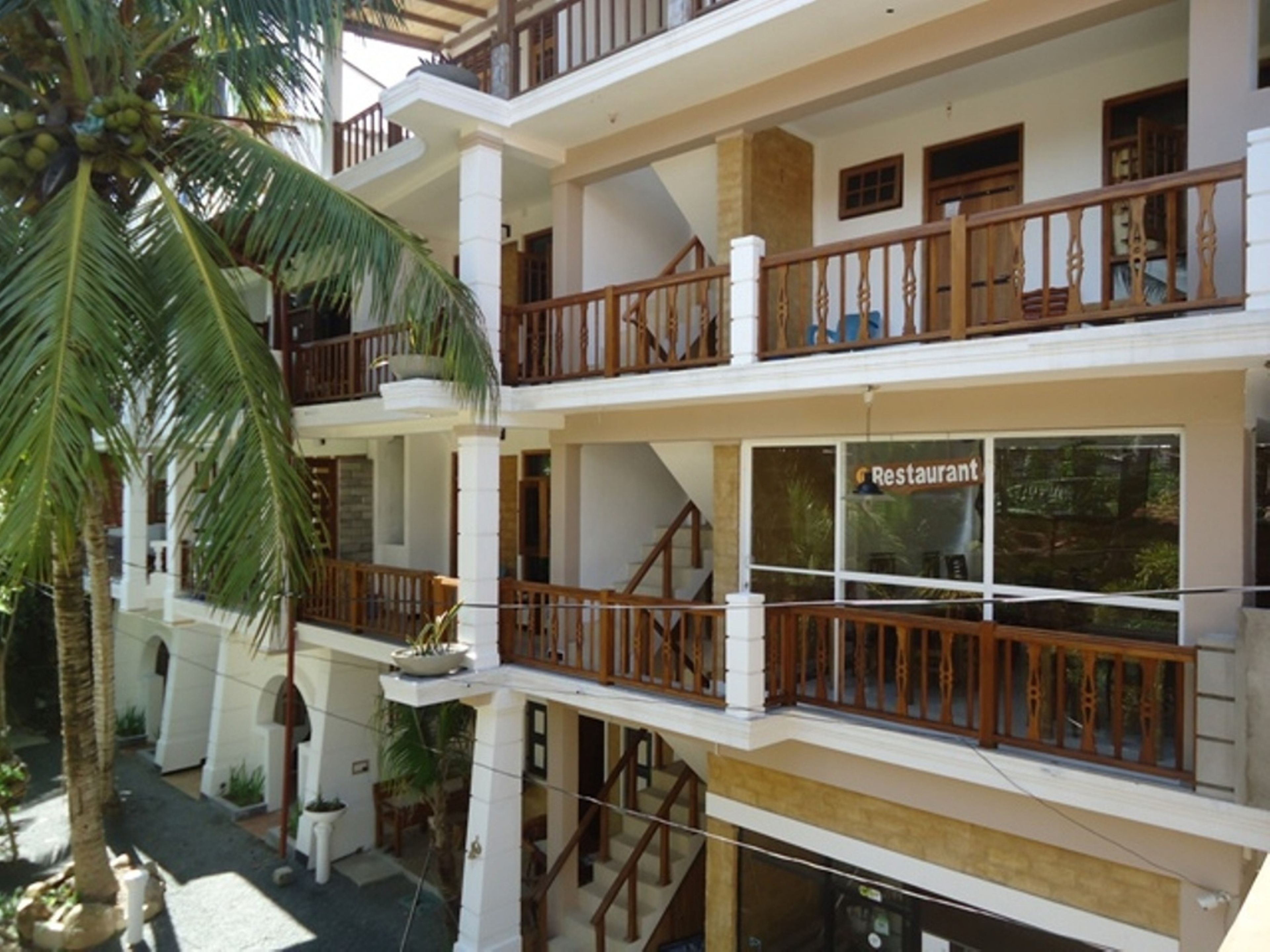 A multi-story hotel with balconies, a restaurant, and a palm tree.