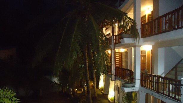 A multi-story hotel with a balcony on the upper floor, palm trees, and outdoor lighting.