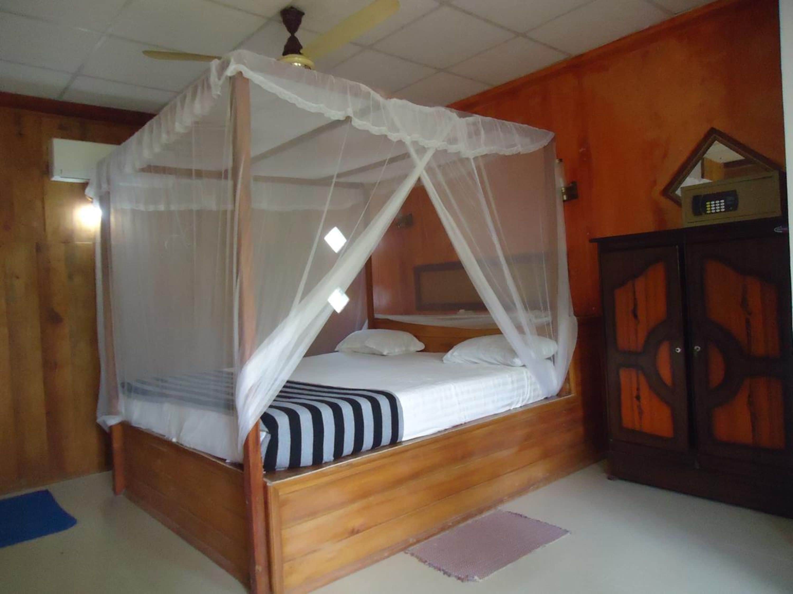 Ein hölzernes Himmelbett mit weißem Moschee, eine Holzkabine mit dekorativer Gestaltung und ein Deckenventilator.