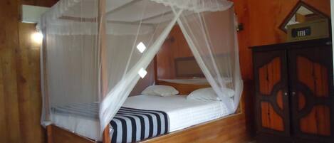 Ein hölzernes Himmelbett mit weißem Moschee, eine Holzkabine mit dekorativer Gestaltung und ein Deckenventilator.