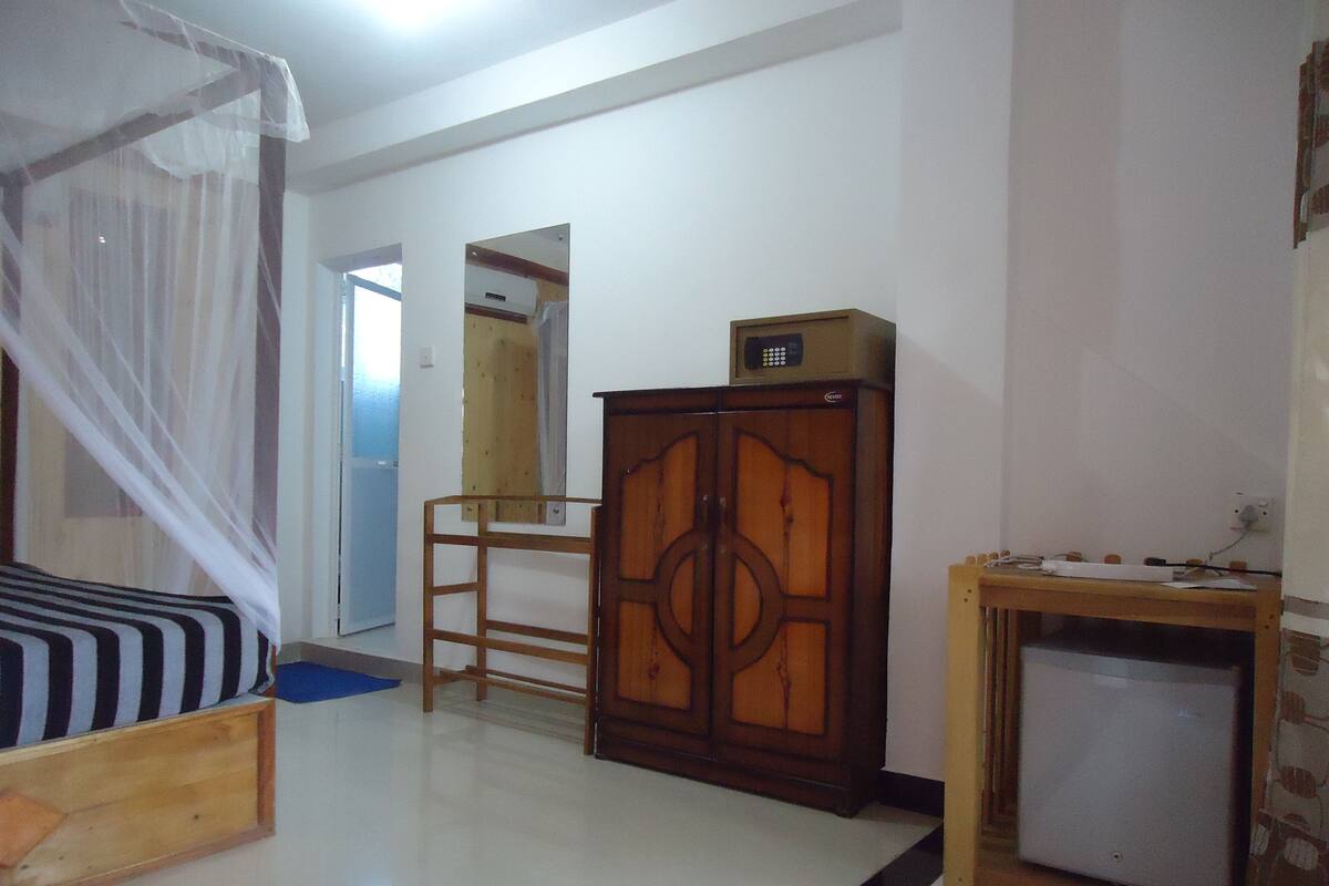A bedroom with a bed, a wooden cabinet, a desk, and a wardrobe.