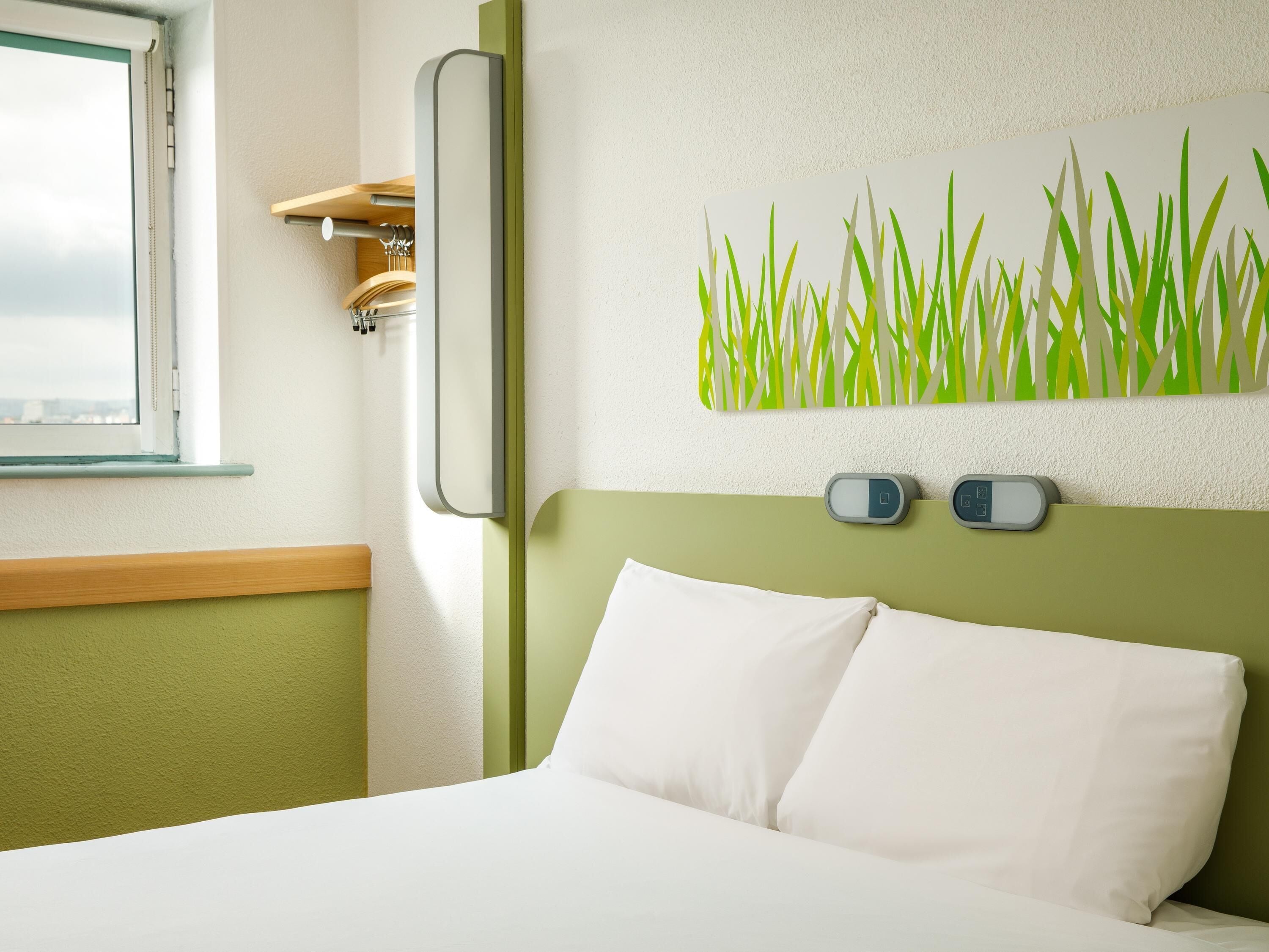 A hotel room with a bed, a wall-mounted clock, and a painting of grass.