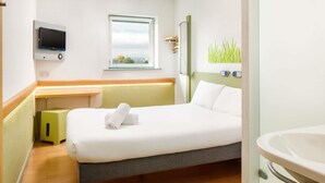 Une chambre d’hôtel avec un lit, un bureau, une télévision, une fenêtre et une salle de bain.