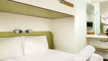 Habitación de hotel con una cama, cabecera verde, mesita de noche con espejo y una toalla blanca.