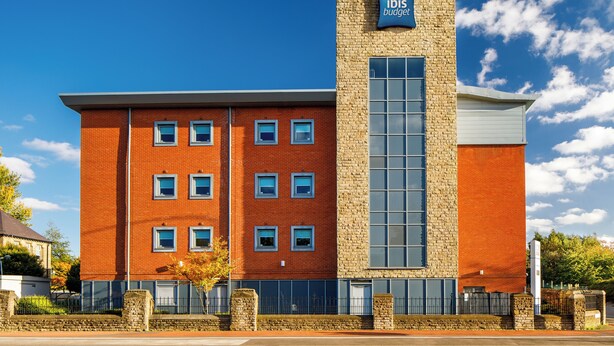 En bygning med flere etager og et tydeligt 'ibis budget' skilt, med en murstensfacade og et stort vindue på højre side.