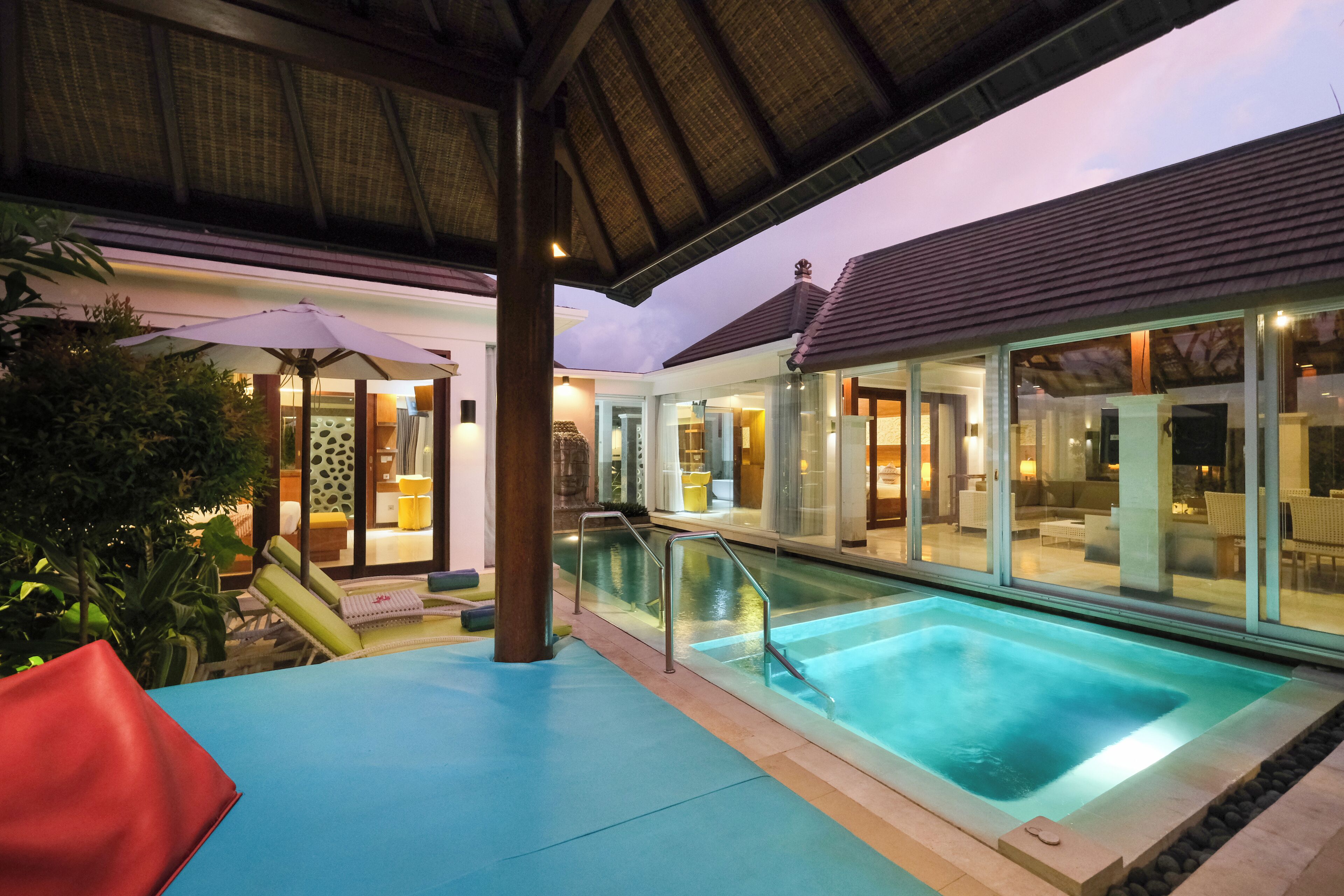An indoor swimming pool area with a glass enclosure, a covered seating area, and a poolside lounge.