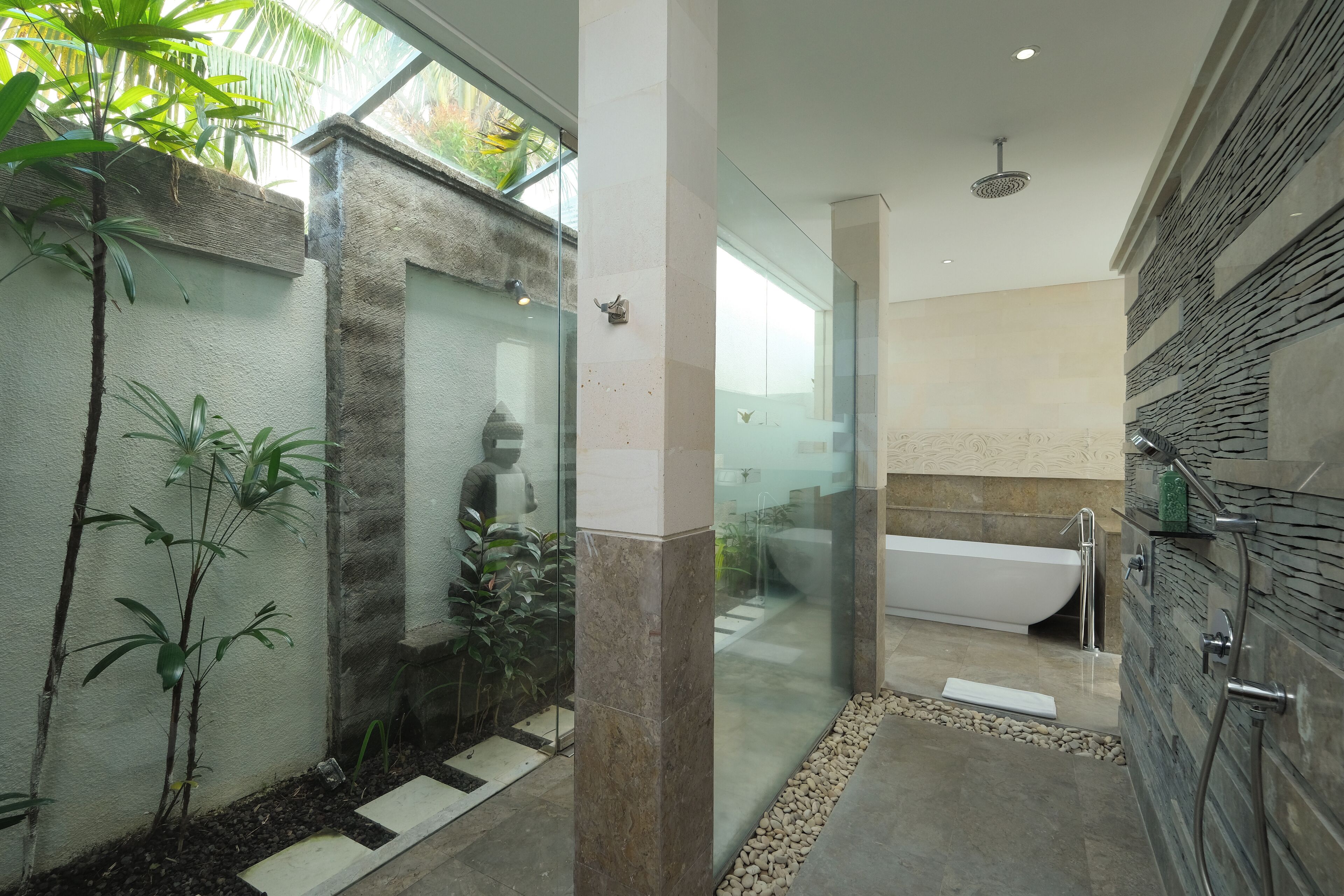 A modern bathroom with a glass shower enclosure, a freestanding bathtub, and a stone wall.