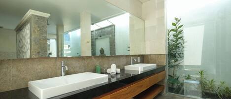 Un baño moderno con un espejo grande, dos lavamanos, tocador de madera y cabina de ducha de vidrio.
