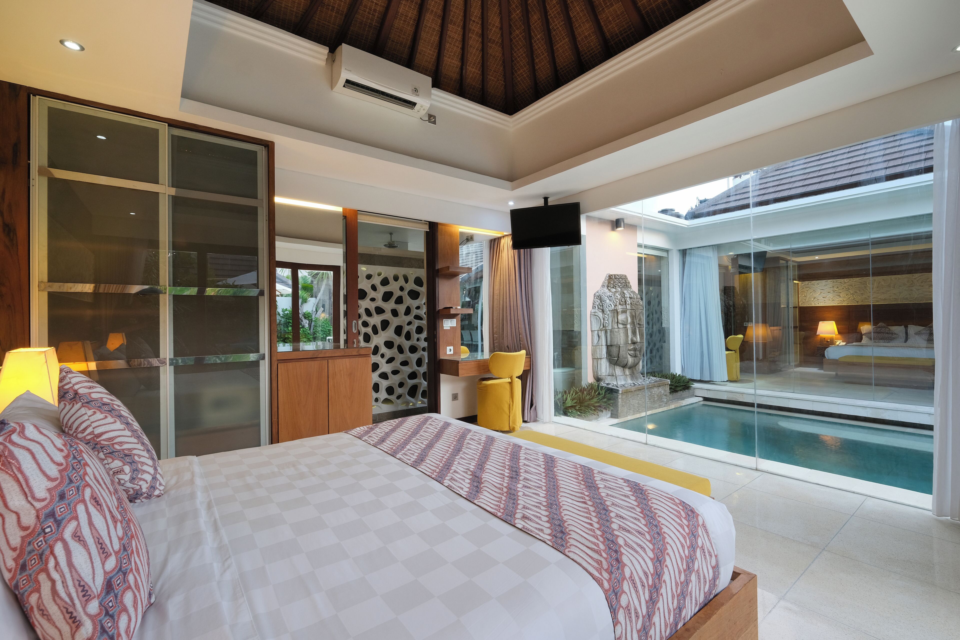 A modern bedroom with a large bed, a glass door leading to a pool, and a flat-screen TV mounted on the wall.