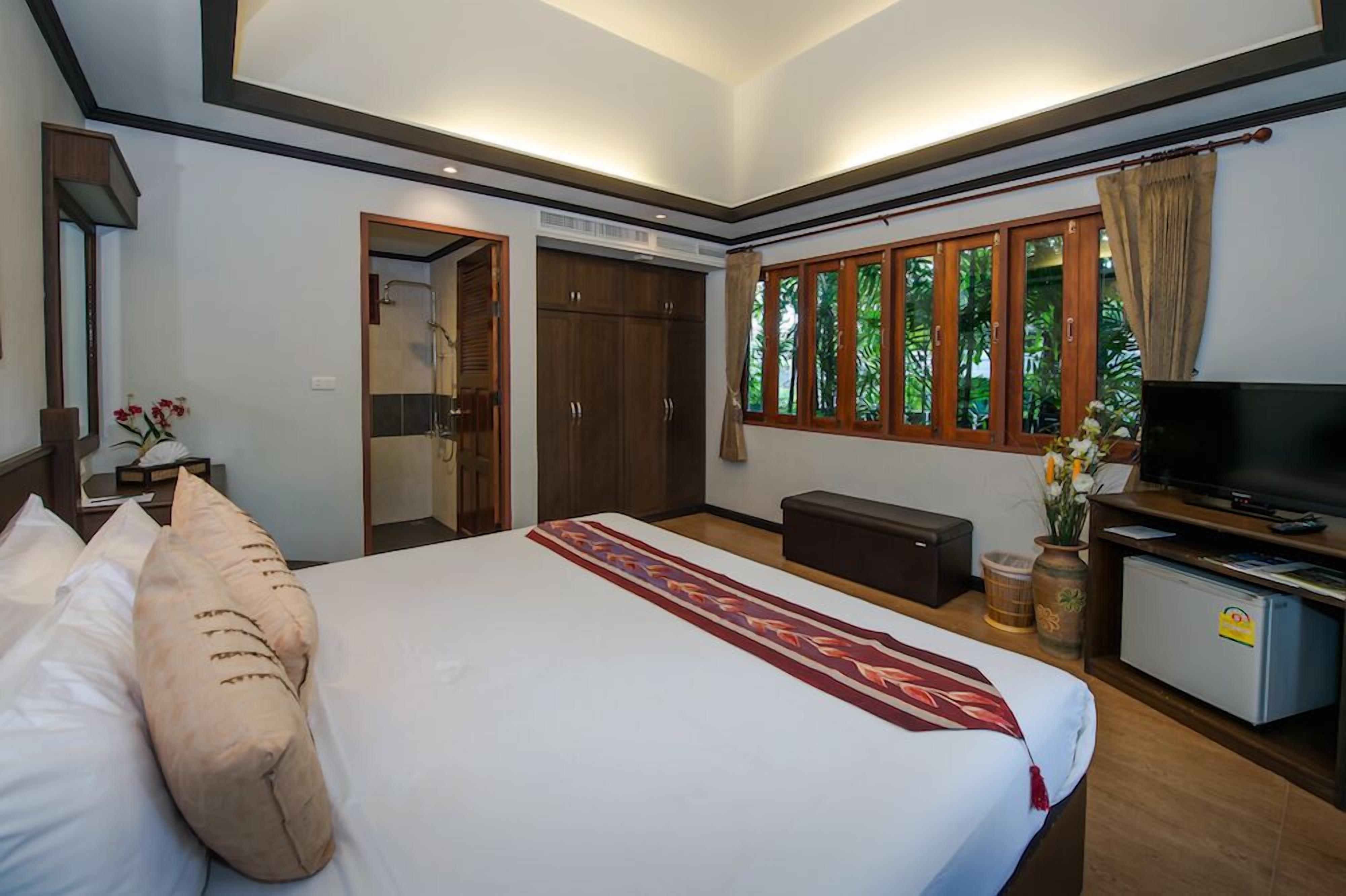 Een slaapkamer met een bed, een televisie, een bureau, een kledingkast en een raam met uitzicht op groen.