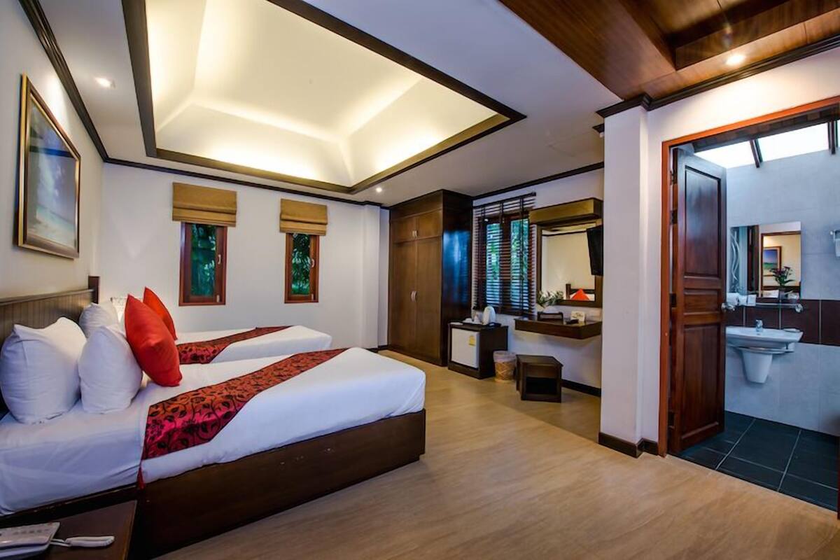 Ein Hotelzimmer mit zwei Betten, einem Schreibtisch, einem Badezimmer mit Waschbecken und einem großen Fenster mit Jalousien.