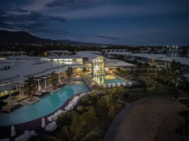 Un resort con varias piscinas, un gran edificio de fachada de vidrio y montañas al fondo.