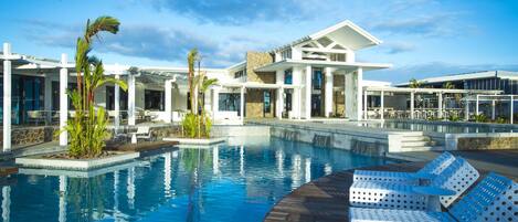 A modern pool area with lounge chairs, a clear pool, and a building with a stone facade.